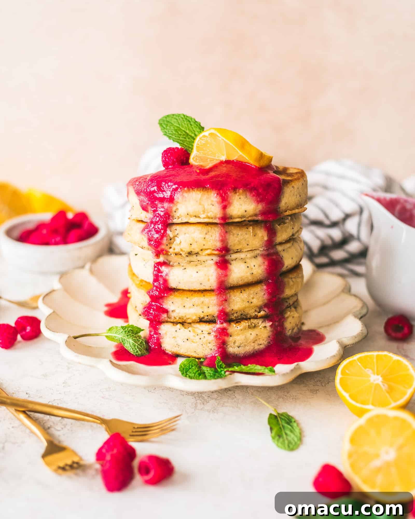 Freshly cooked lemon poppy seed pancakes on a plate, surrounded by lemons and raspberries