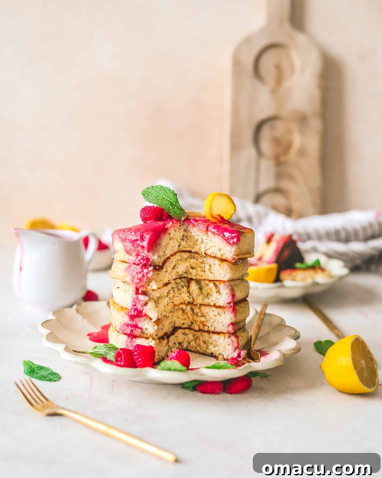 Overhead shot of a full plate of lemon poppy seed pancakes, with a spoon of raspberry coulis and fresh fruits