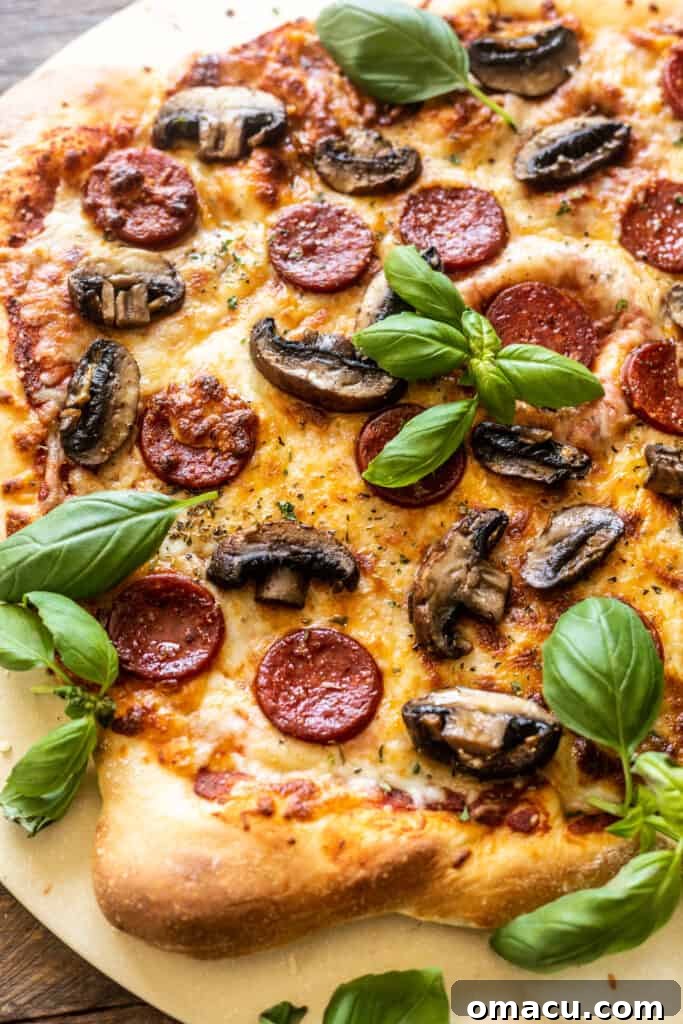 A freshly baked roasted mushroom and pepperoni pizza on a pizza stone, garnished with fresh herbs.
