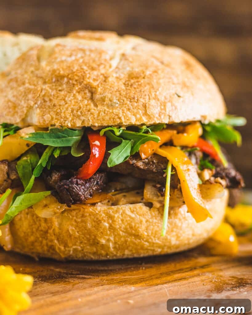 Ingredients for a Cajun steak sandwich laid out on a wooden cutting board, including thinly sliced ribeye, bell peppers, onions, and ciabatta bread.