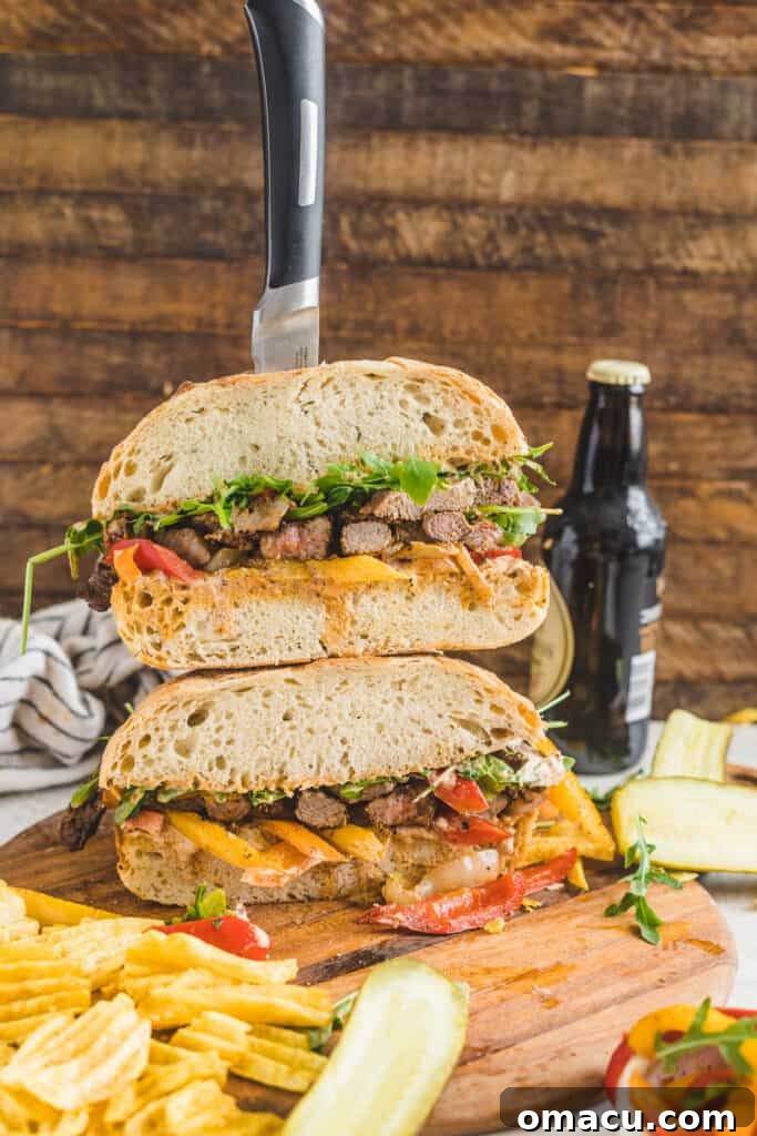 Overhead view of a finished Cajun steak sandwich, highlighting the layers of thinly sliced steak, colorful peppers and onions, and fresh arugula on ciabatta bread.