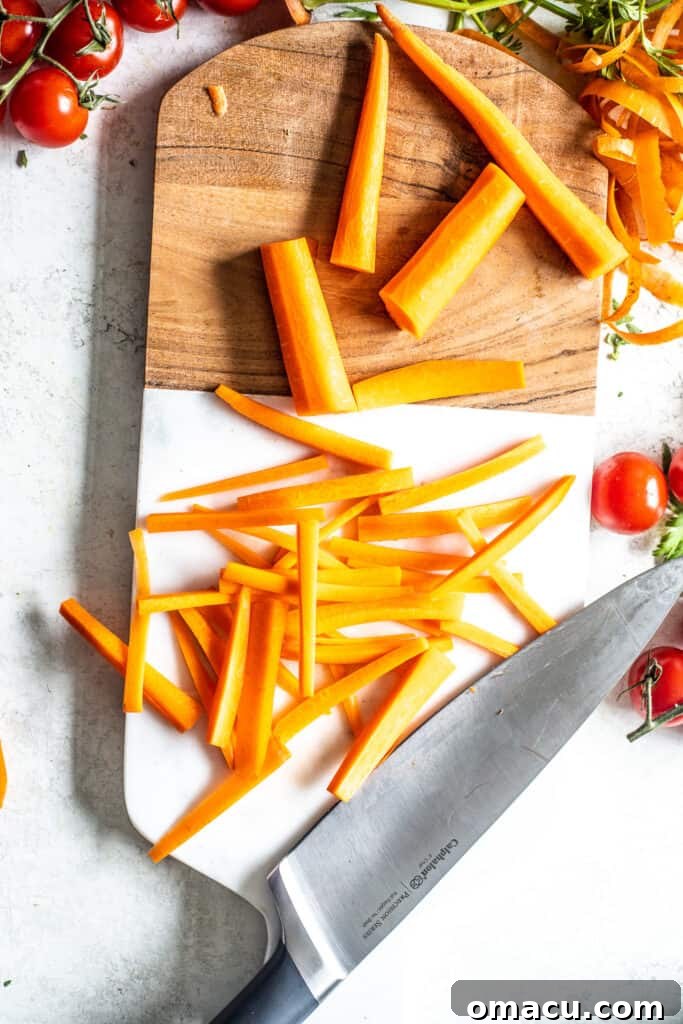 Stacked carrot planks being cut into matchsticks on a cutting board