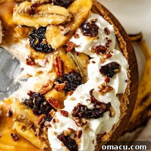 A beautifully decorated Bananas Foster Cheesecake on a cake stand, topped with glossy caramelized bananas, succulent prunes, and airy cinnamon whipped cream, ready to be served.