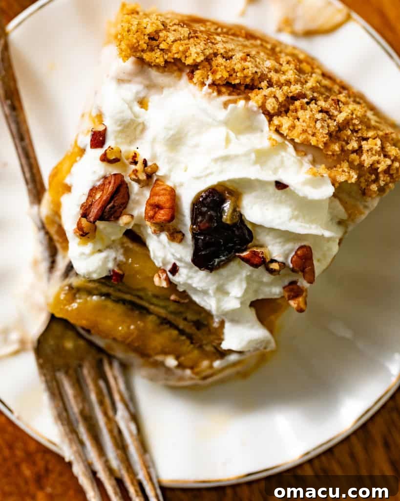 A perfectly portioned slice of Bananas Foster Cheesecake rests on a white plate, its layers visible and adorned with rich caramel sauce and banana slices. A fork is poised beside it, inviting a taste.