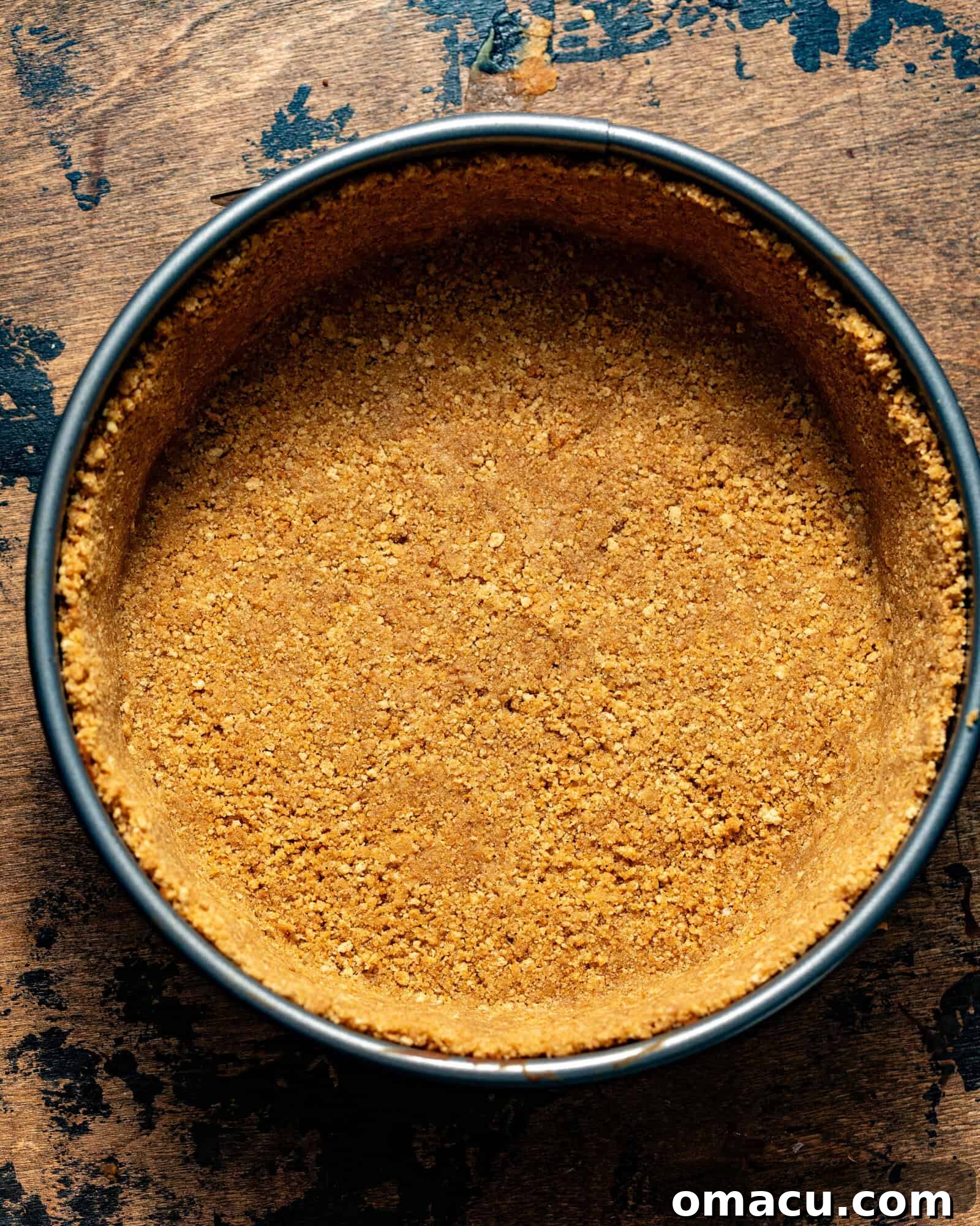A freshly baked and cooled graham cracker crust sits in a springform pan, ready for the cheesecake batter. Its golden brown edges and firm base promise a perfect foundation for the creamy filling.