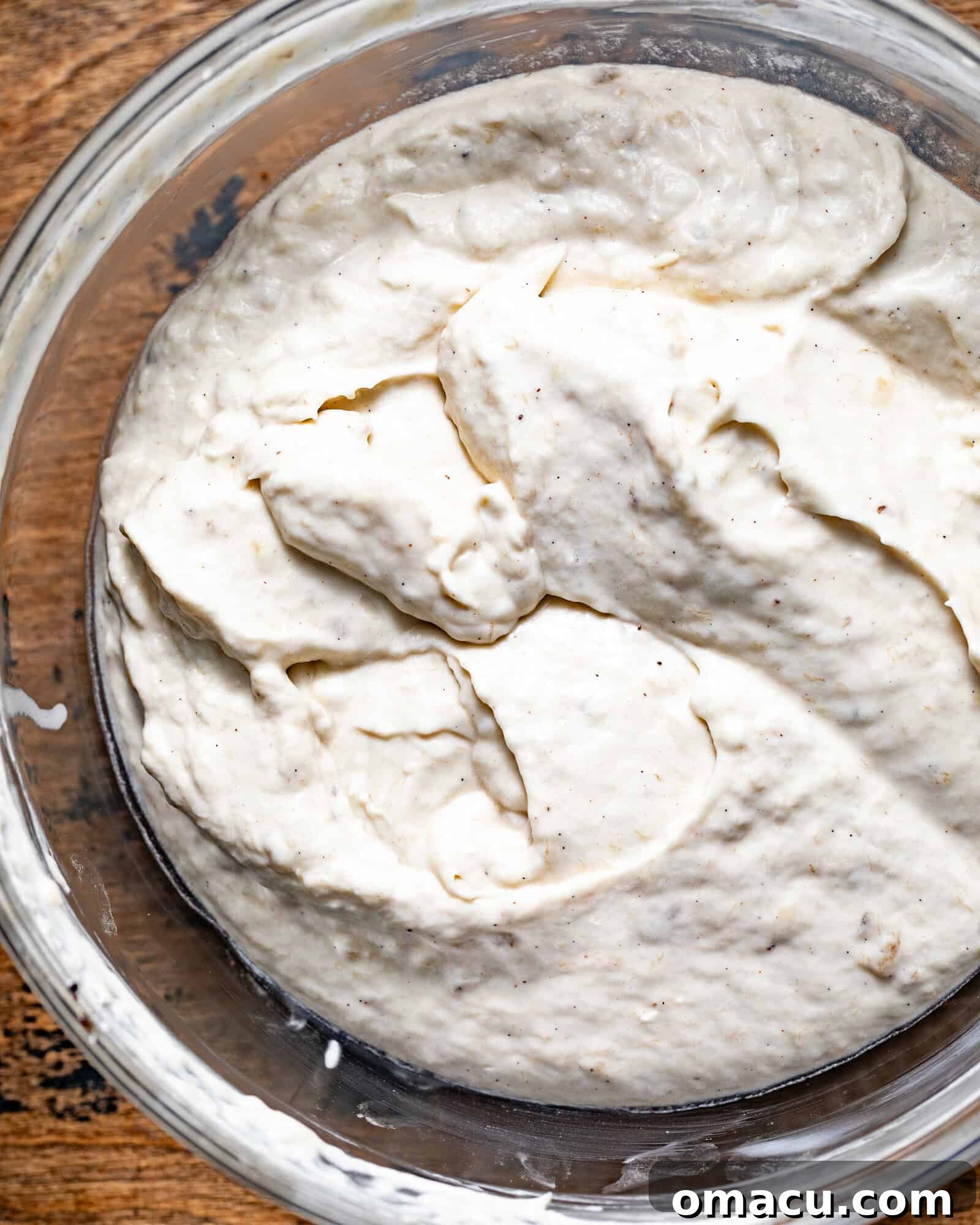 Close-up of creamy cheesecake batter in a stand mixer bowl, showing the smooth blend of cream cheese, sugar, vanilla, and eggs, before the addition of bananas, hinting at the rich base of the dessert.