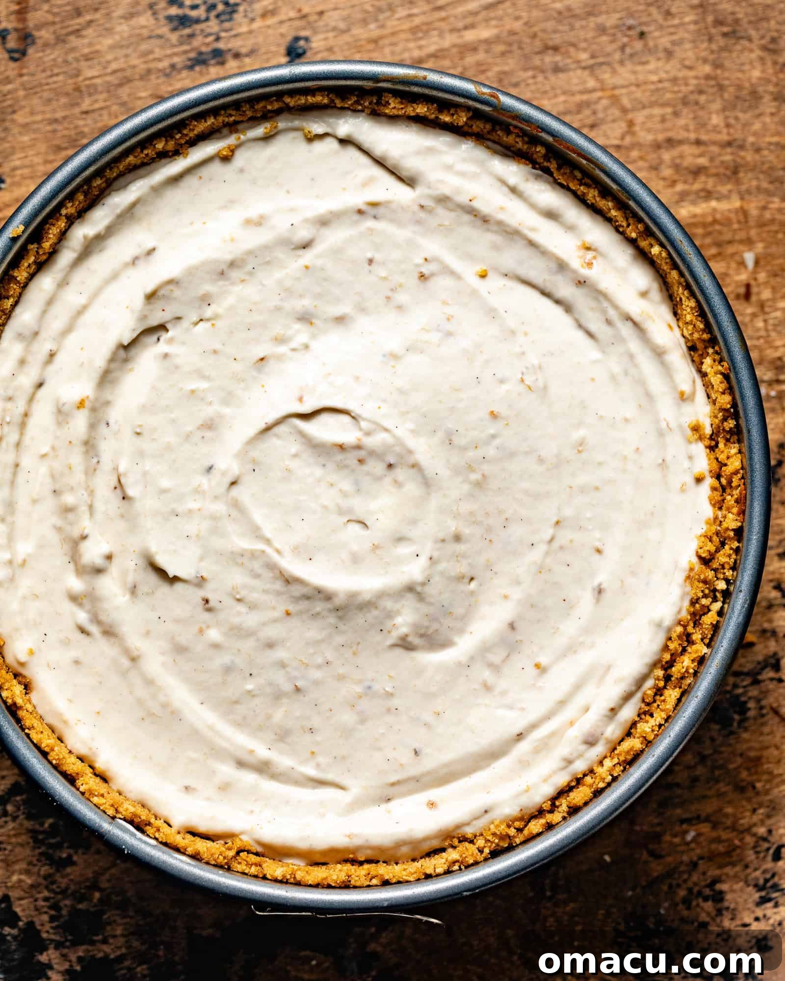 The smooth, creamy banana cheesecake batter fills the golden graham cracker crust in a springform pan, perfectly level and ready for its journey into the oven, hinting at the delicious dessert to come.