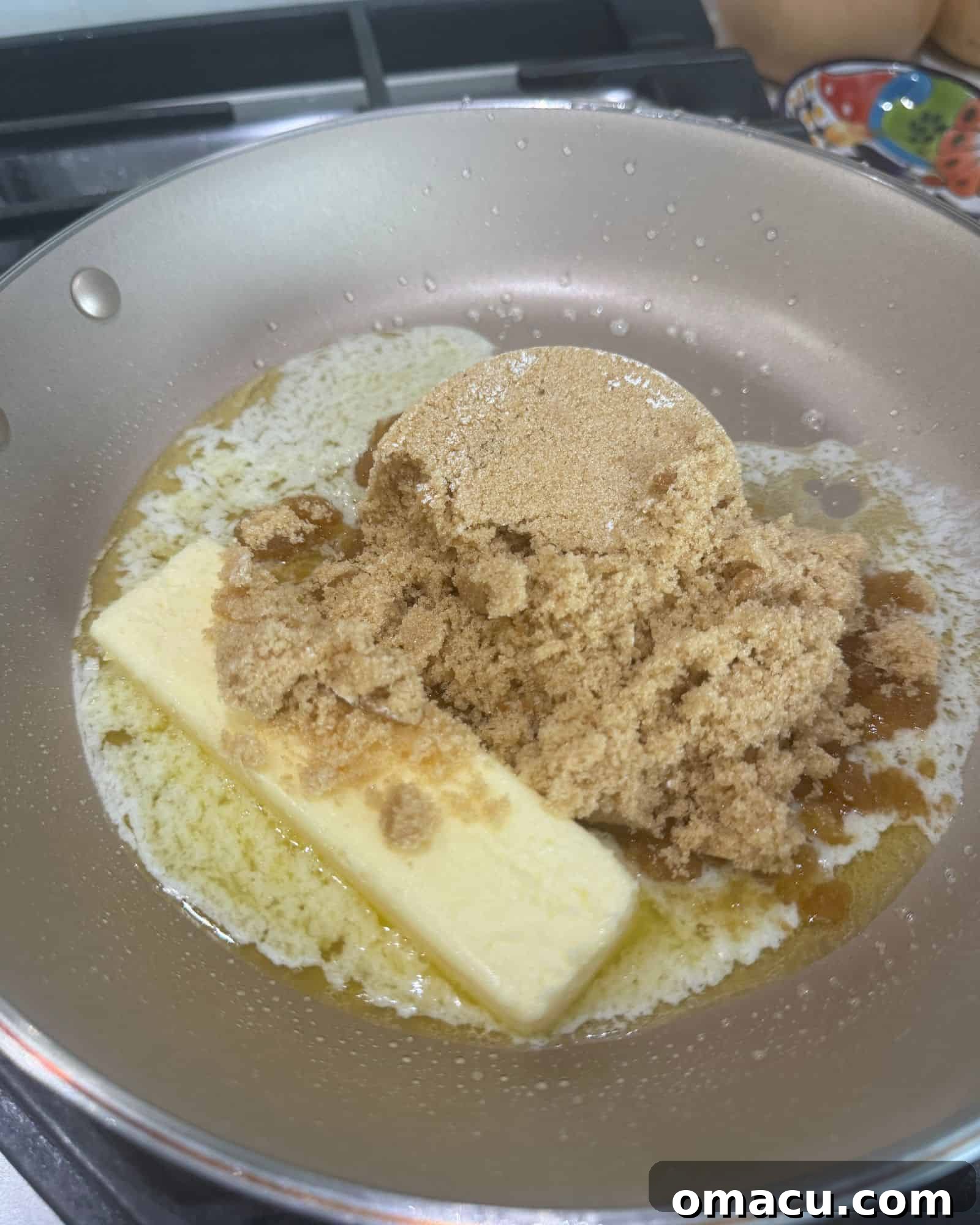 Close-up of butter and brown sugar melting together in a nonstick skillet over medium heat, forming the base of a rich, golden caramel sauce, with a spatula stirring the mixture to ensure even melting.
