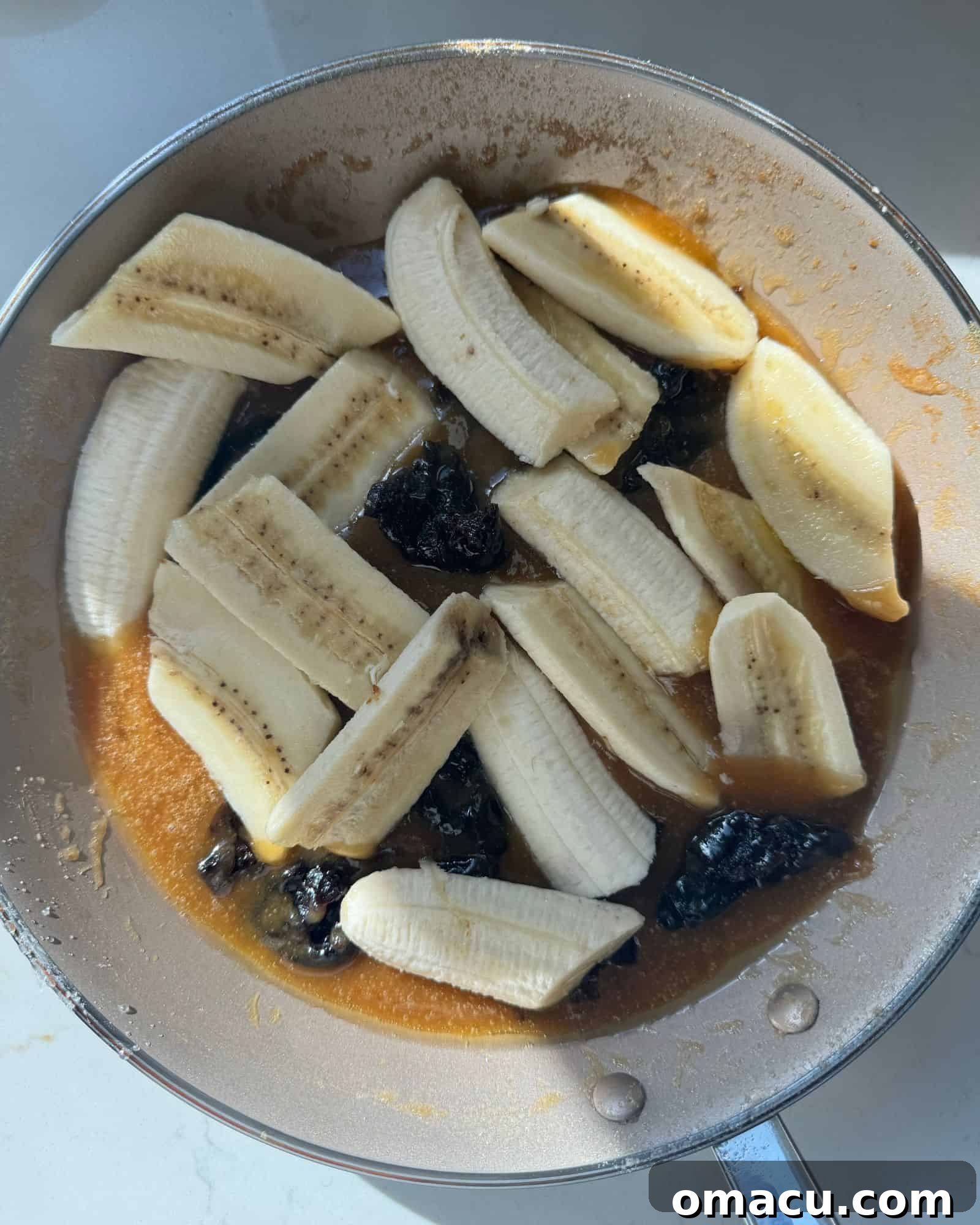 Caramelized bananas and chopped prunes simmering in a bubbling brown sugar and whiskey caramel sauce in a nonstick skillet, the ingredients glistening and releasing their aromas, ready to top the cheesecake.