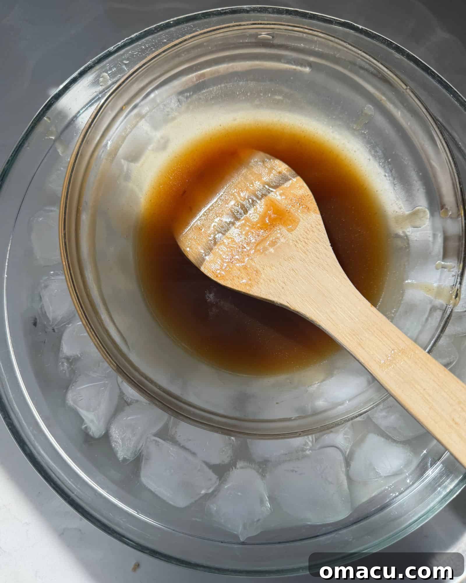 A heat-safe bowl containing the rich, dark whiskey brown sugar caramel sauce with prunes is nestled into a larger bowl filled with ice water, rapidly cooling the topping to the perfect consistency for the cheesecake.