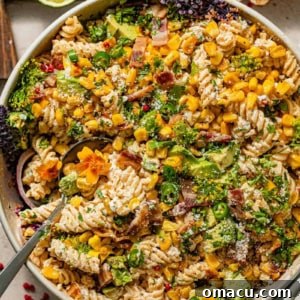 Elote pasta salad in a large bowl topped with roasted corn, bacon, jalapenos, red onions, and cilantro.