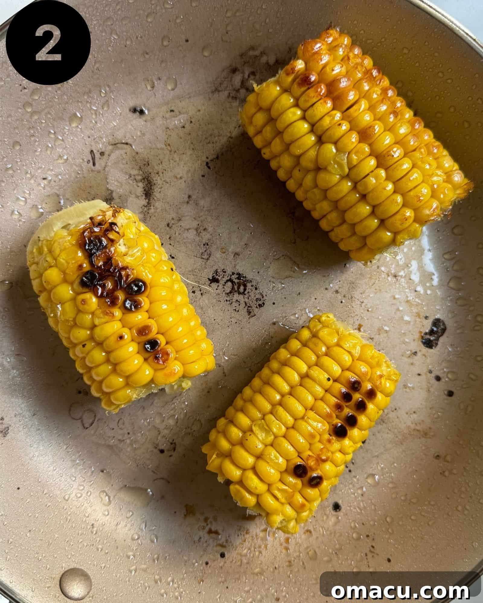 Corn kernels searing in a skillet, developing a slight char.