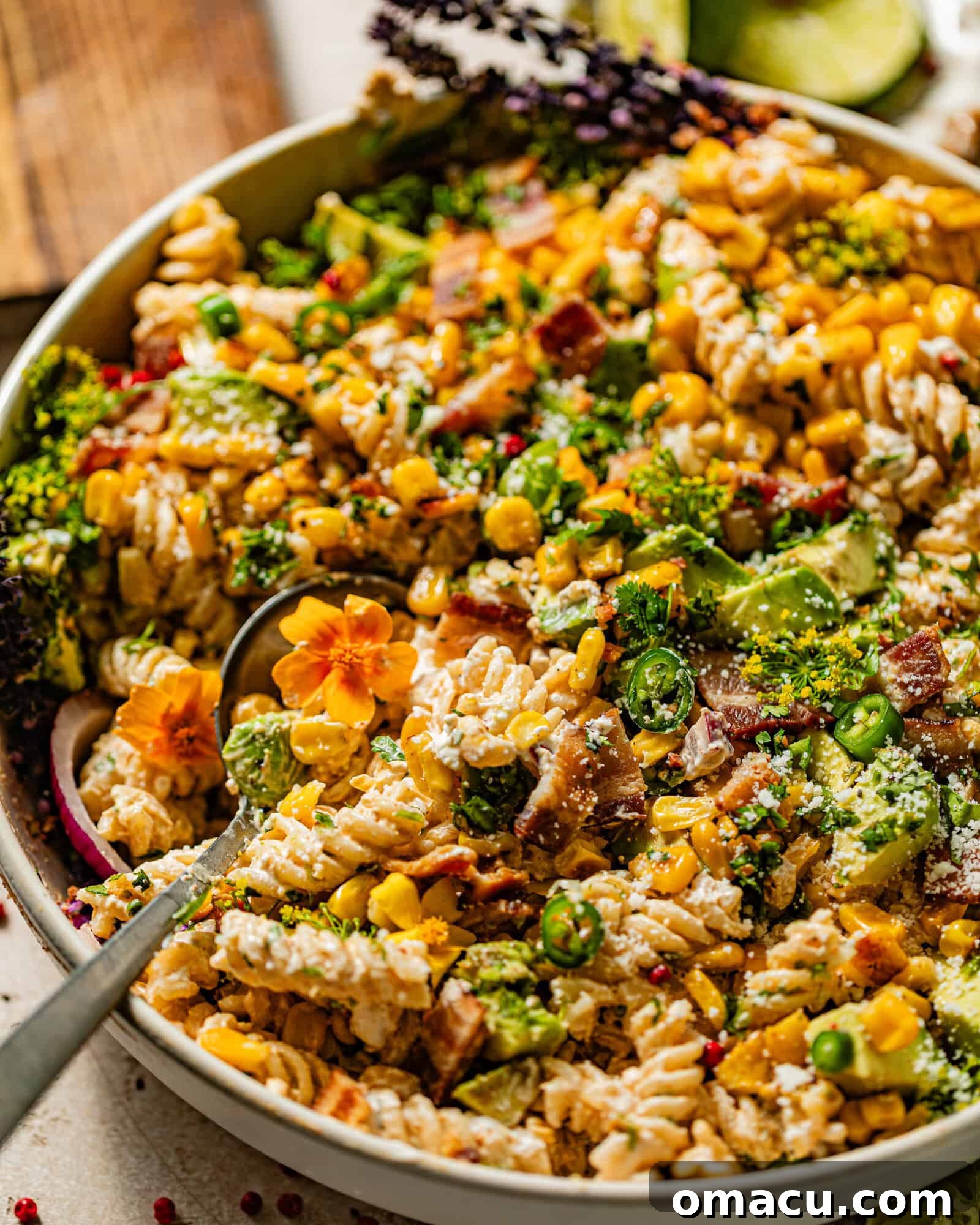 The finished Elote pasta salad presented in a bowl on a serving board, accompanied by a spoon.