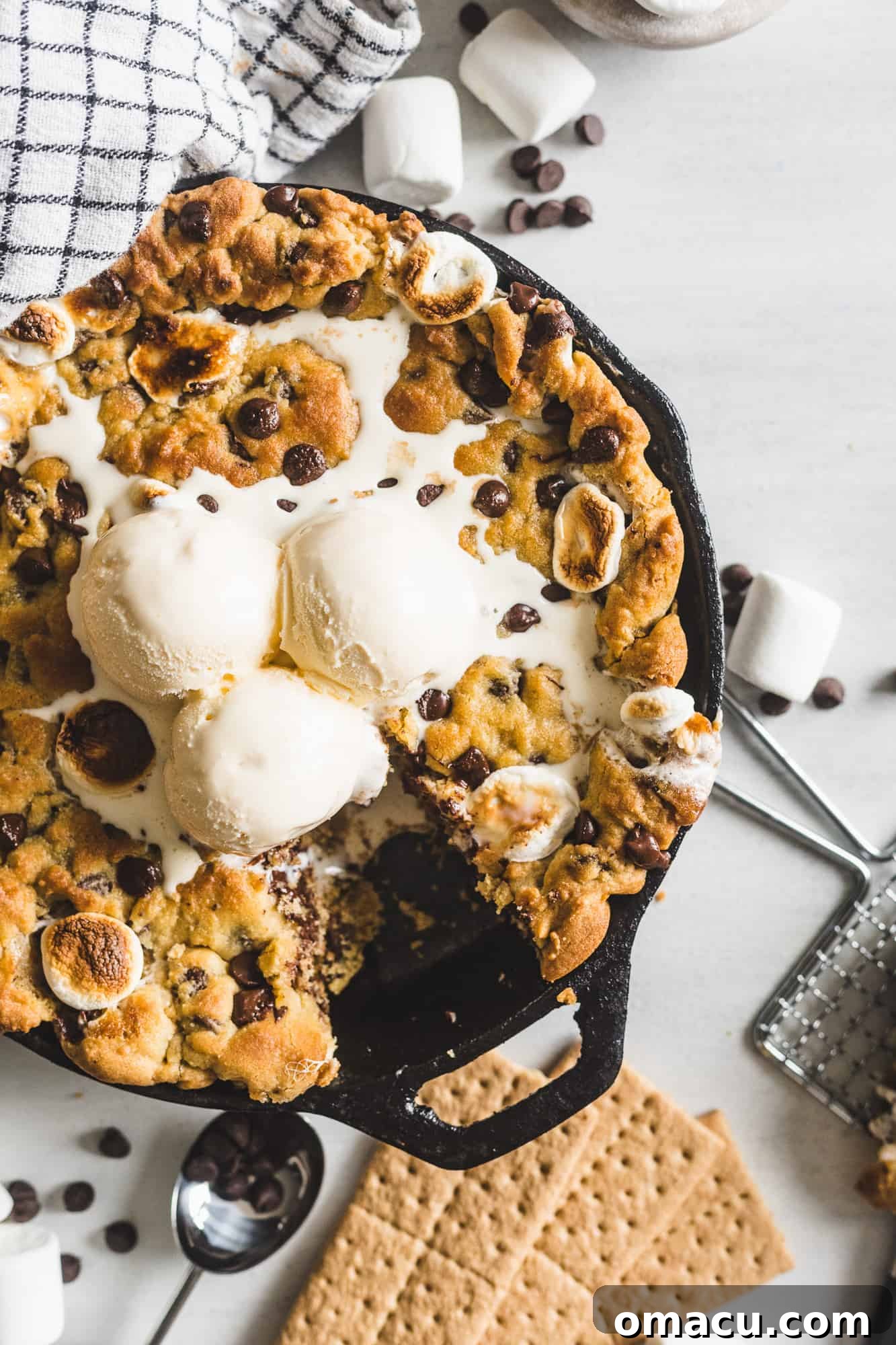 Decadent S'mores Stuffed Chocolate Chip Skillet Cookie topped with a scoop of vanilla ice cream, showcasing its gooey marshmallow and melted chocolate center.