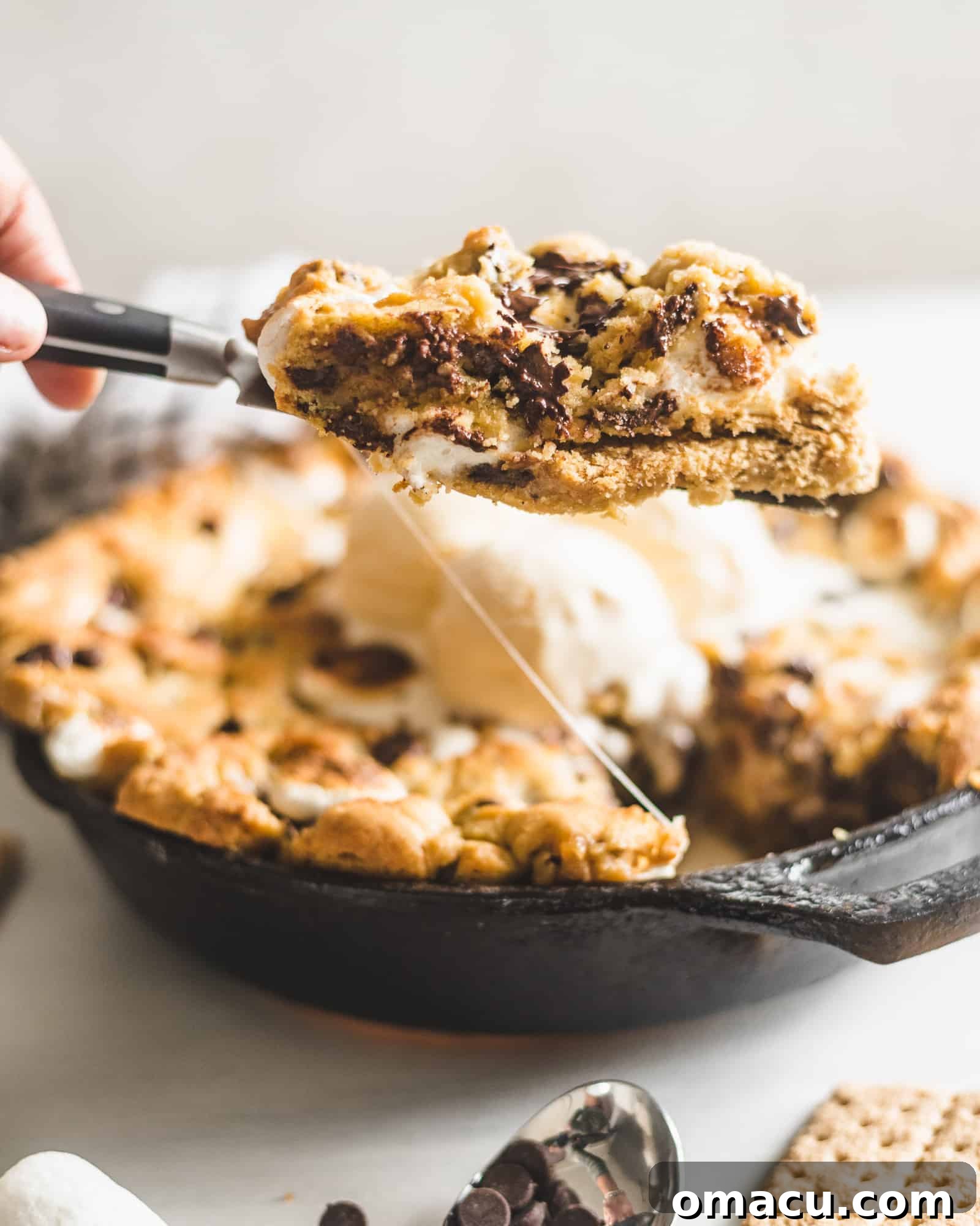 S'mores Stuffed Chocolate Chip Skillet Cookie, half eaten, revealing its layers of marshmallow, chocolate, and graham cracker.