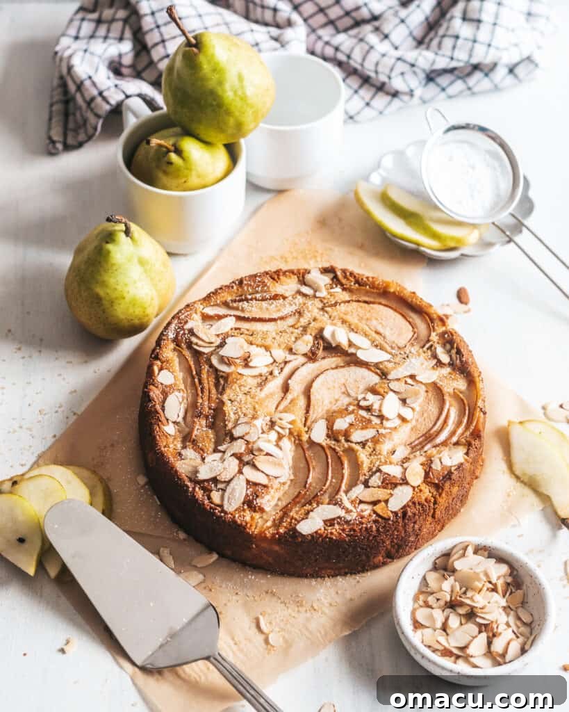 A beautifully decorated Spiced Pear and Almond Cake on a white surface, surrounded by fresh pears, highlighting its rustic elegance.