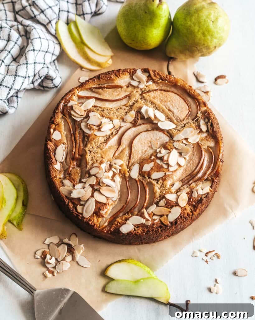 The Spiced Pear and Almond Cake presented whole on a white surface, with fresh pears artfully arranged around it.