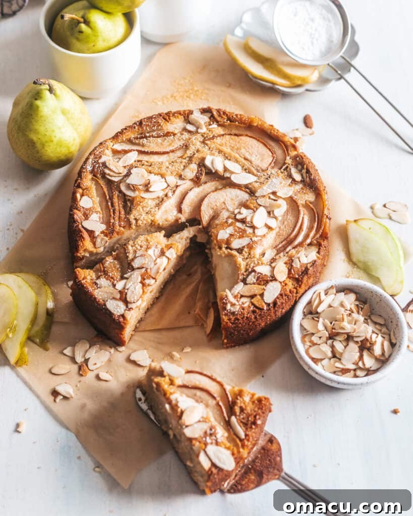 A whole Spiced Pear and Almond Cake, sliced almonds visible on top, with decorative pears arranged on the side.