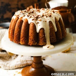 Carrot cake bundt cake on a cake stand with maple brown butter cream cheese frosting and chopped pecans on top.
