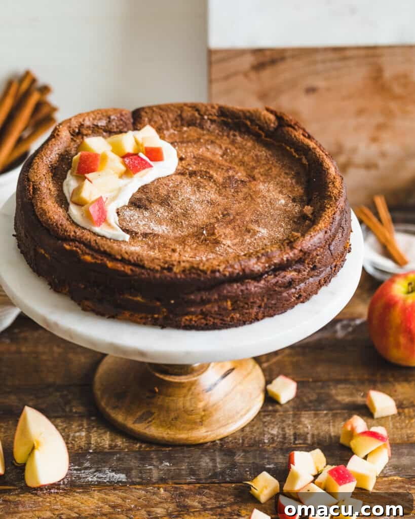 A decadent Apple Butter Basque Cheesecake on a cake stand, artfully topped with whipped ricotta and caramelized apple slices, ready to be enjoyed.