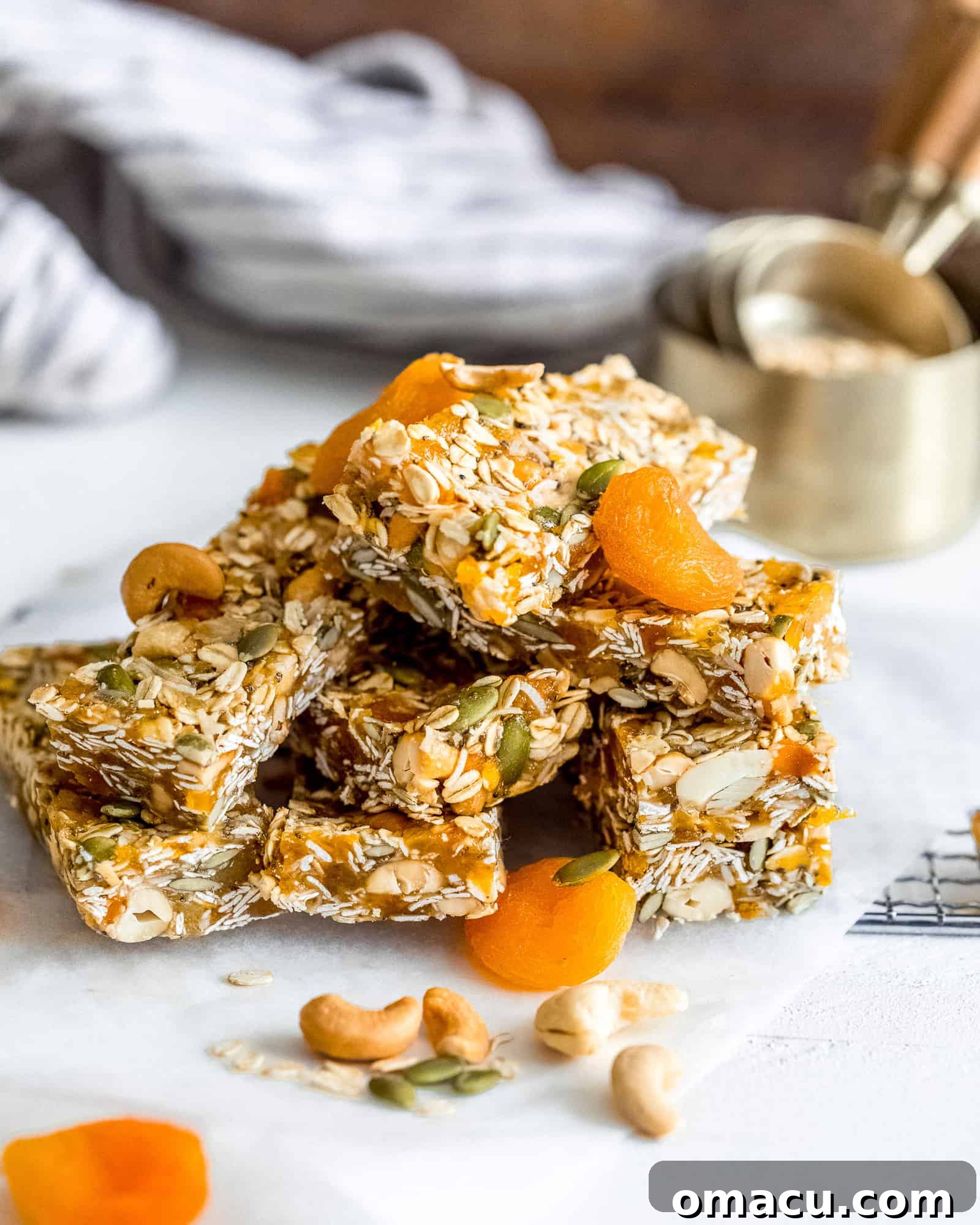A stack of Apricot Coconut Cashew Bars rests beside a measuring cup filled with rolled oats, emphasizing the key ingredients for this healthy snack.