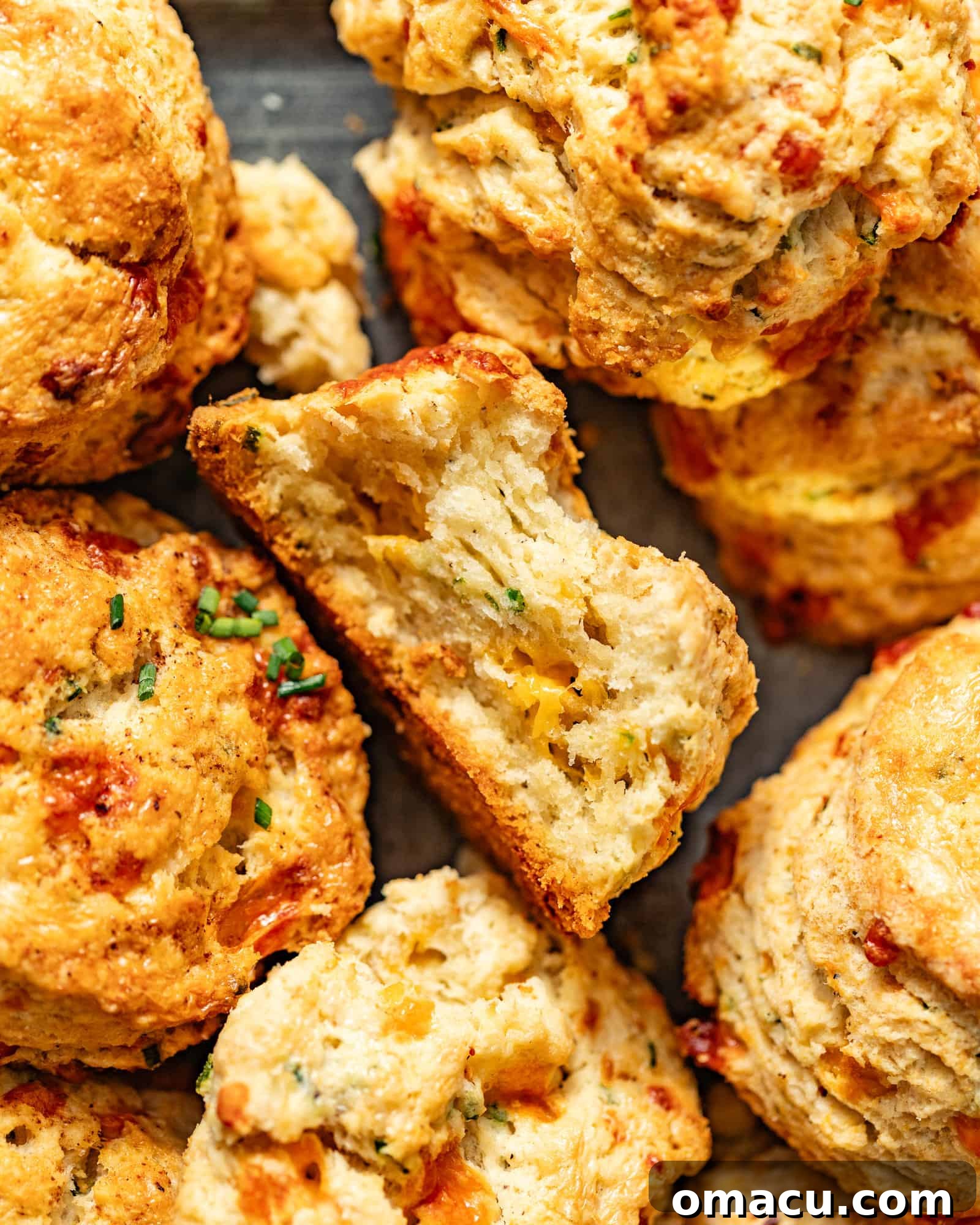 up close photo of cheddar biscuits with chives on a serving tray with one biscuit with a bite taken out of it.