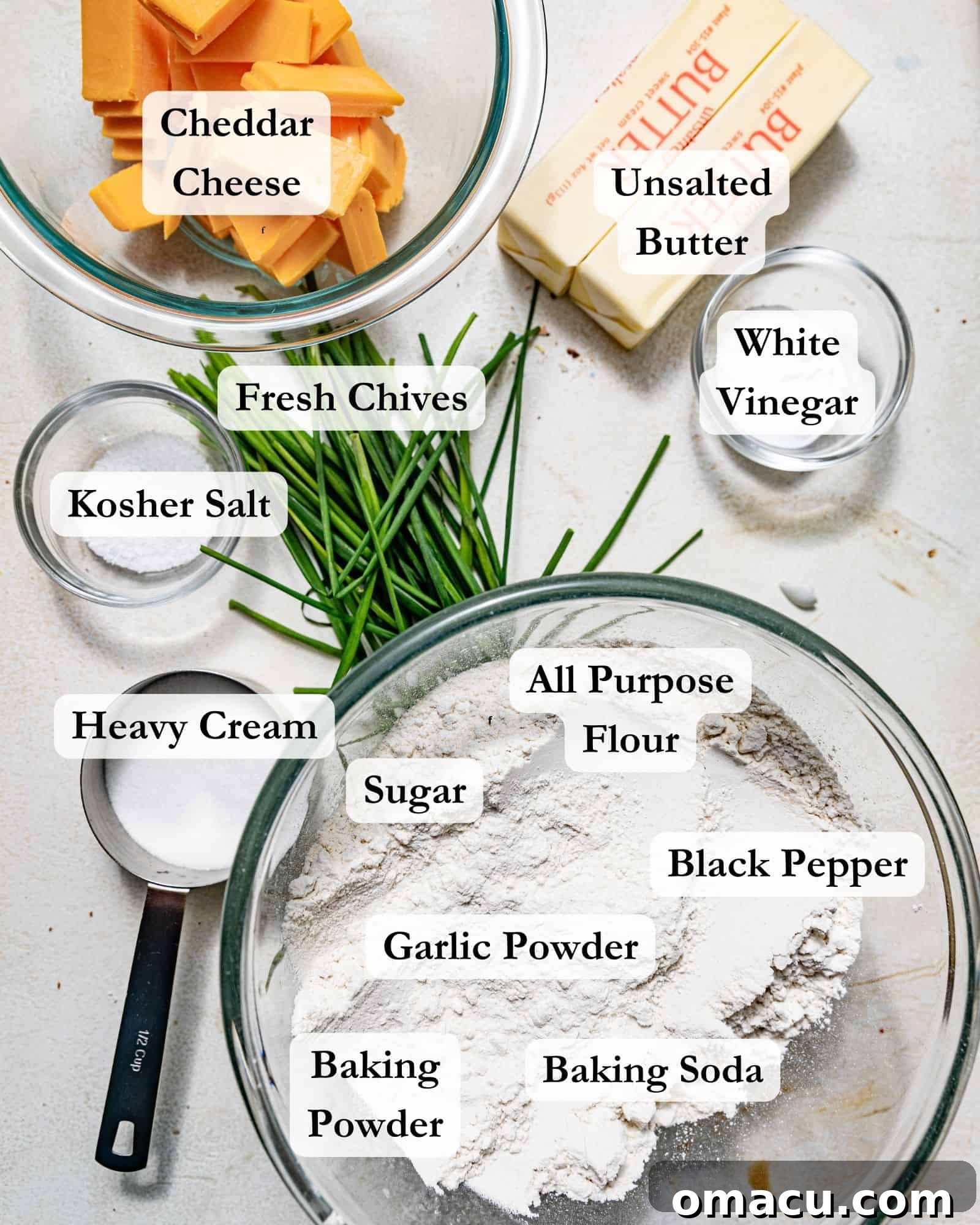 ingredients to make cheddar biscuits - flour, sugar, salt, pepper, garlic powder, baking powder, baking soda, chives, cheddar cheese, butter, heavy cream, and vinegar.