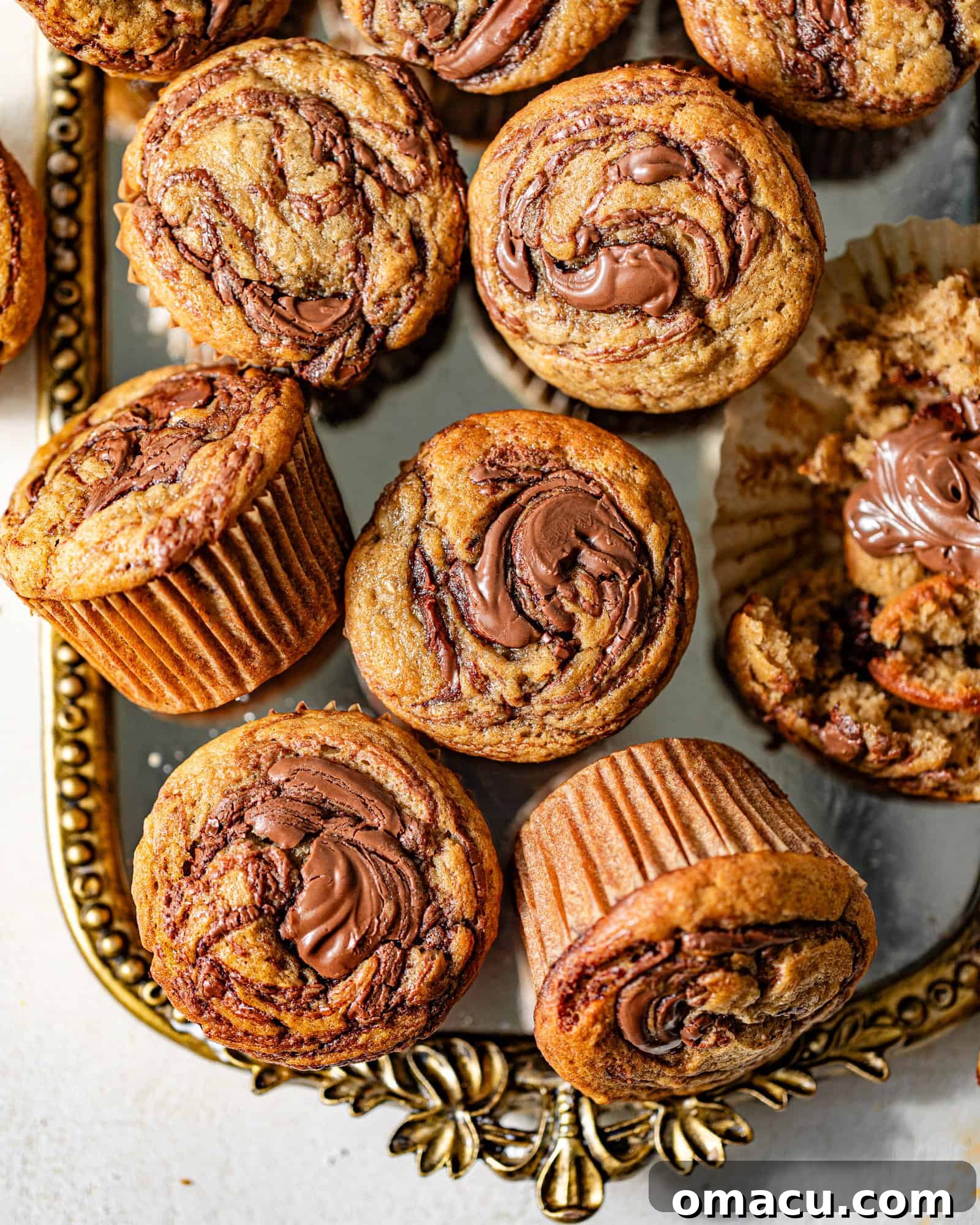 Golden brown banana Nutella muffins arranged artfully on a gold mirror tray, showcasing their perfect domed tops and visible Nutella swirls.