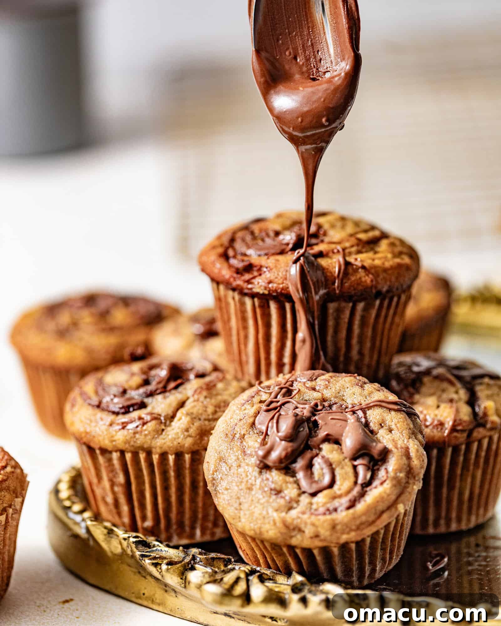 A spoon drizzling rich, melted Nutella over the golden tops of freshly baked banana muffins, adding an extra layer of decadence.