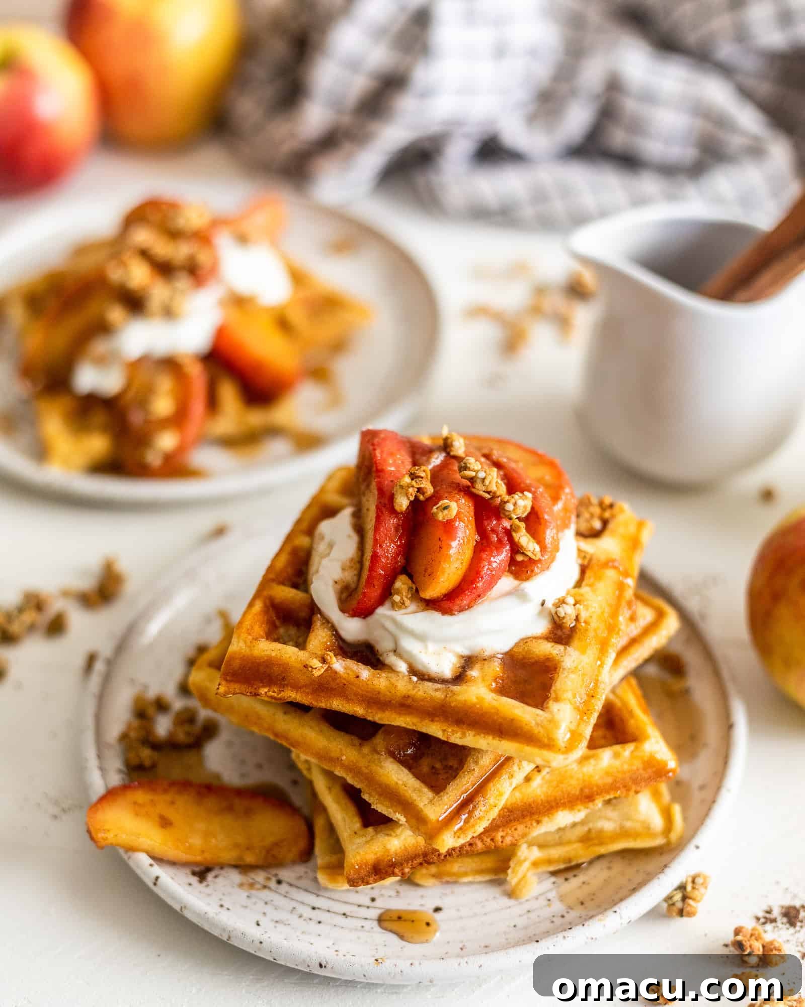 Waffles on a plate with syrup, and more waffles in the background