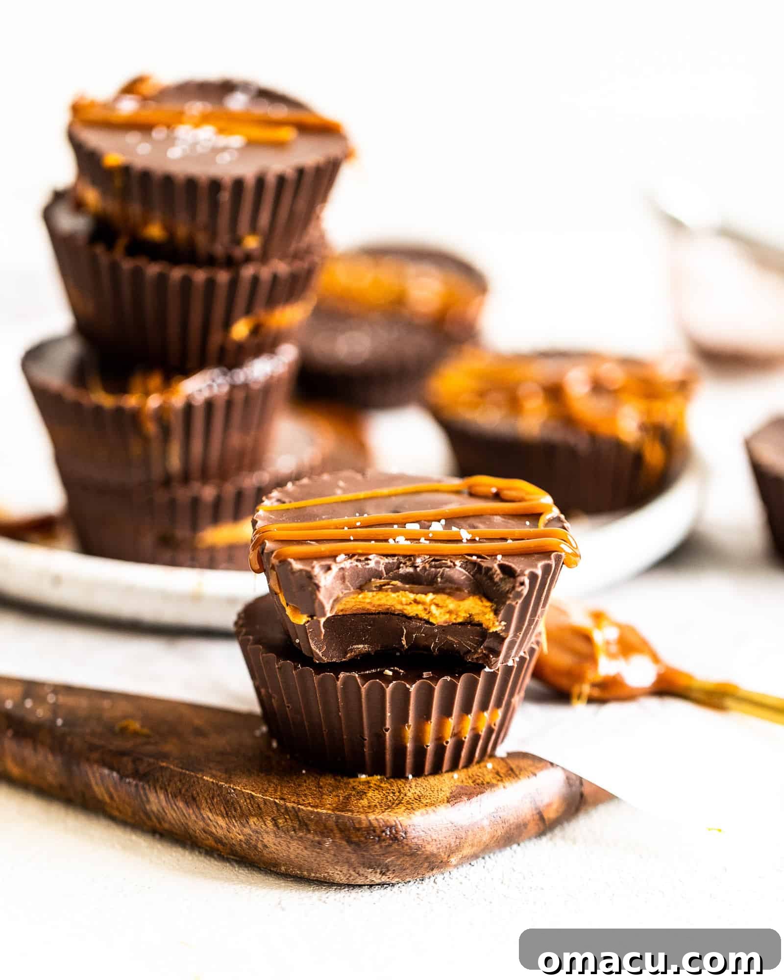 Stacked salted caramel peanut butter cups, glistening with caramel, with more treats artfully arranged in the background.