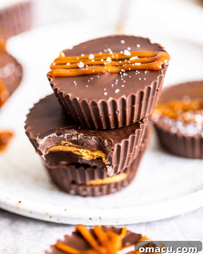 Three perfectly stacked salted caramel peanut butter cups, each adorned with a shimmering caramel drizzle, highlighting their irresistible nature.