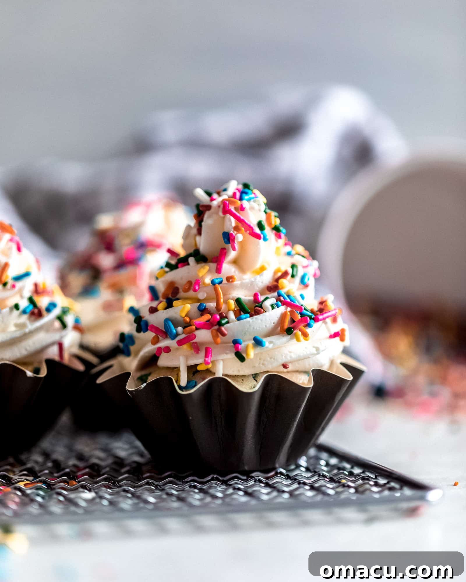 Close-up view of a Funfetti Cupcake generously frosted with almond buttercream and decorated with rainbow sprinkles.