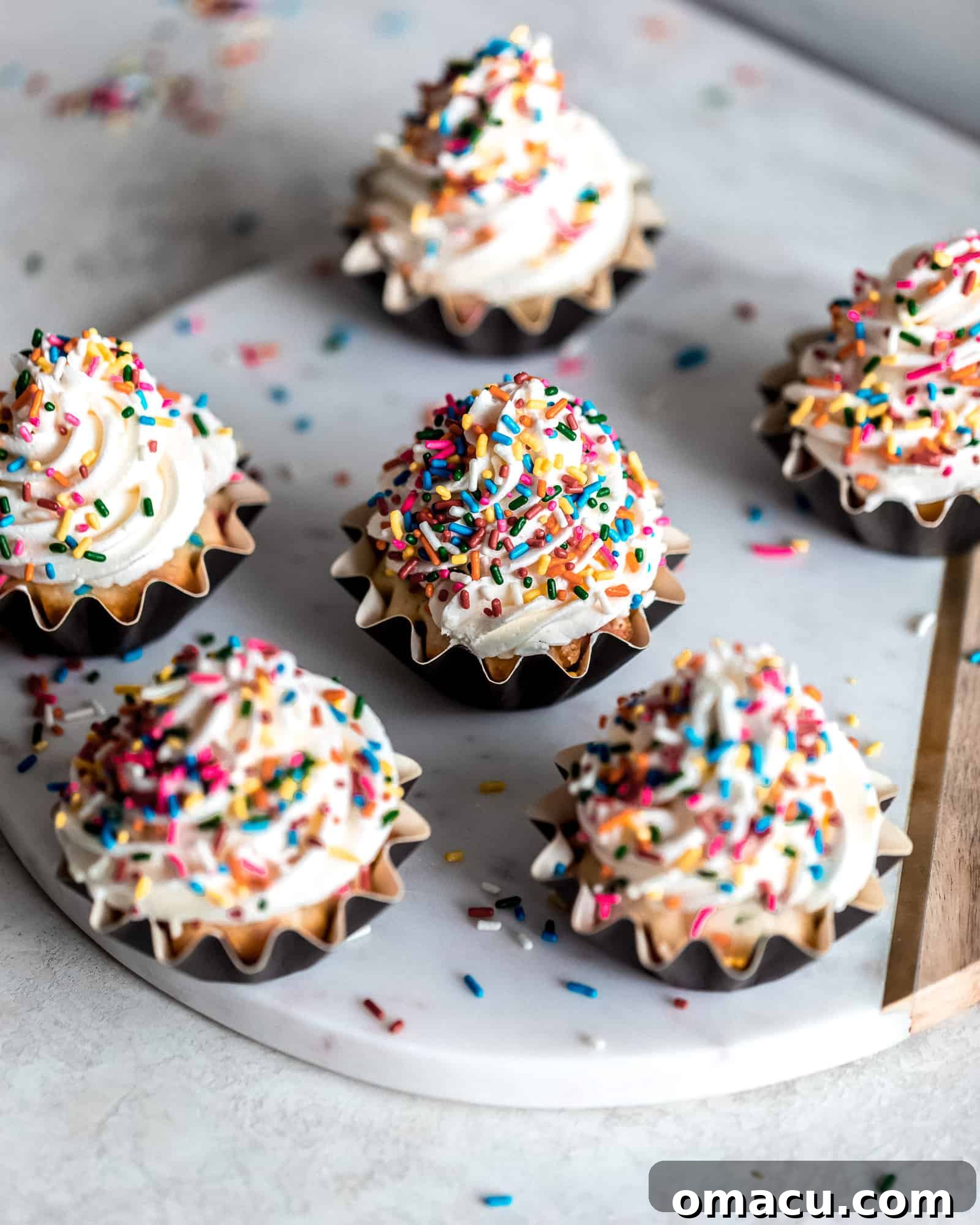 A trio of Funfetti Cupcakes with Almond Buttercream artfully arranged on a rustic marble cutting board.