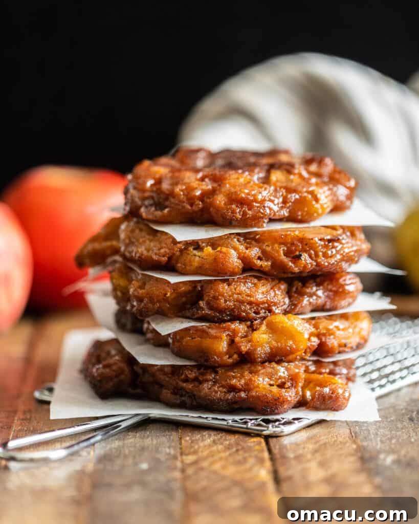 Several apple pear fritters stacked on top of each other with apples and pears blurred in the background.