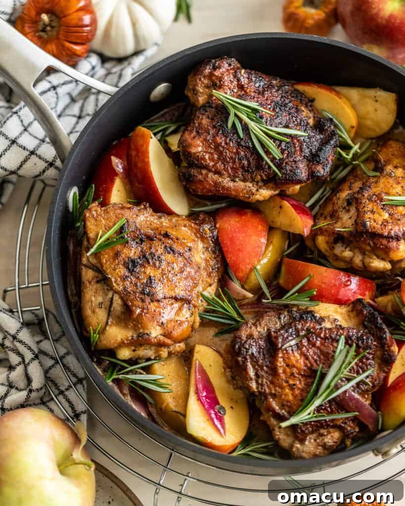 Rosemary Apple Cider Chicken, beautifully golden brown, nestled in a cast iron pan with caramelized apples and red onions, ready to be served.