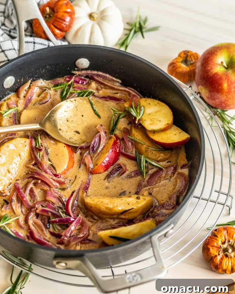 A close-up shot of the rich, golden apple cider sauce bubbling gently in a pan, infused with garlic and rosemary.