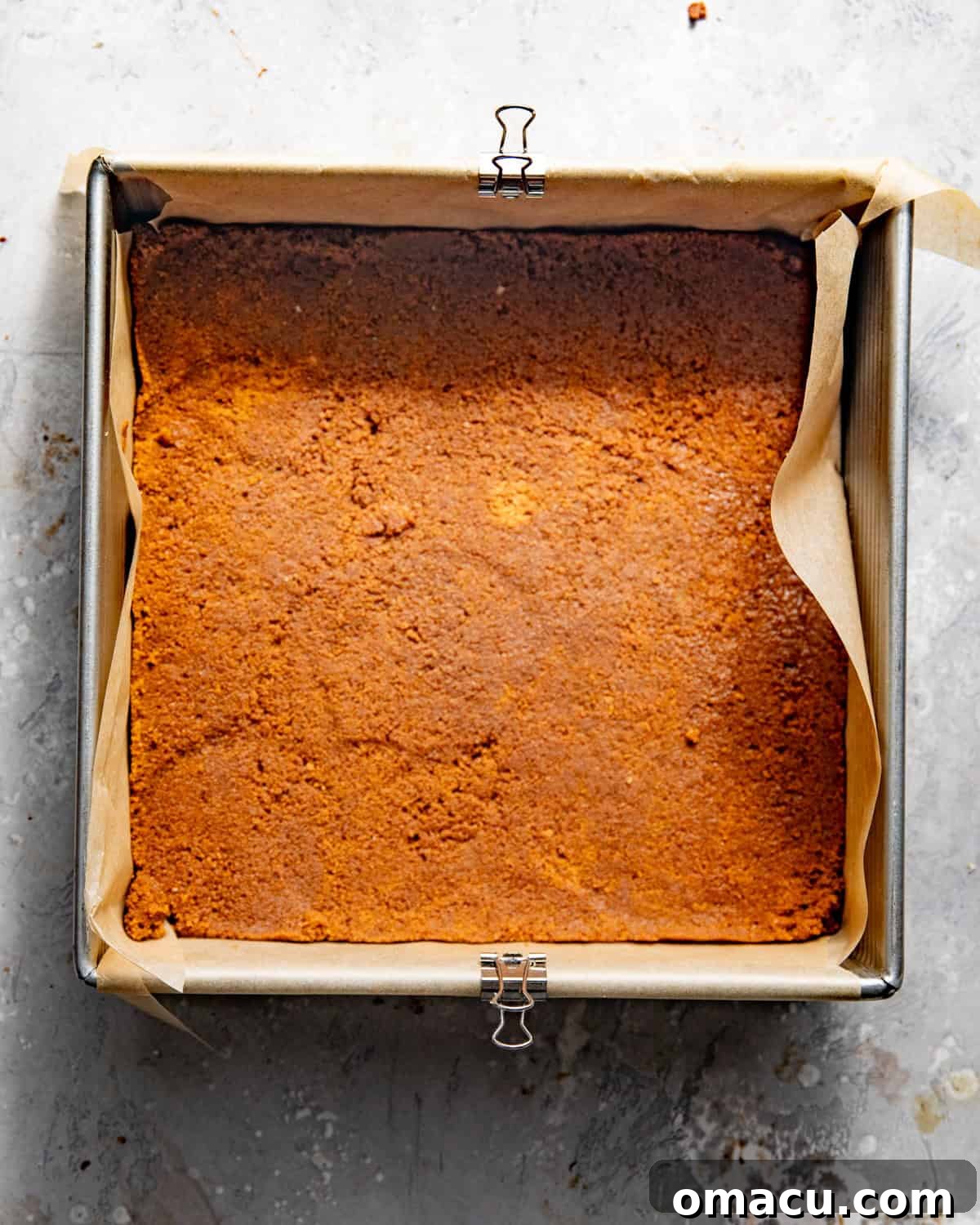 Biscoff cookie crust pressed evenly into a single layer in a 9x9 inch baking pan, lined with parchment paper.