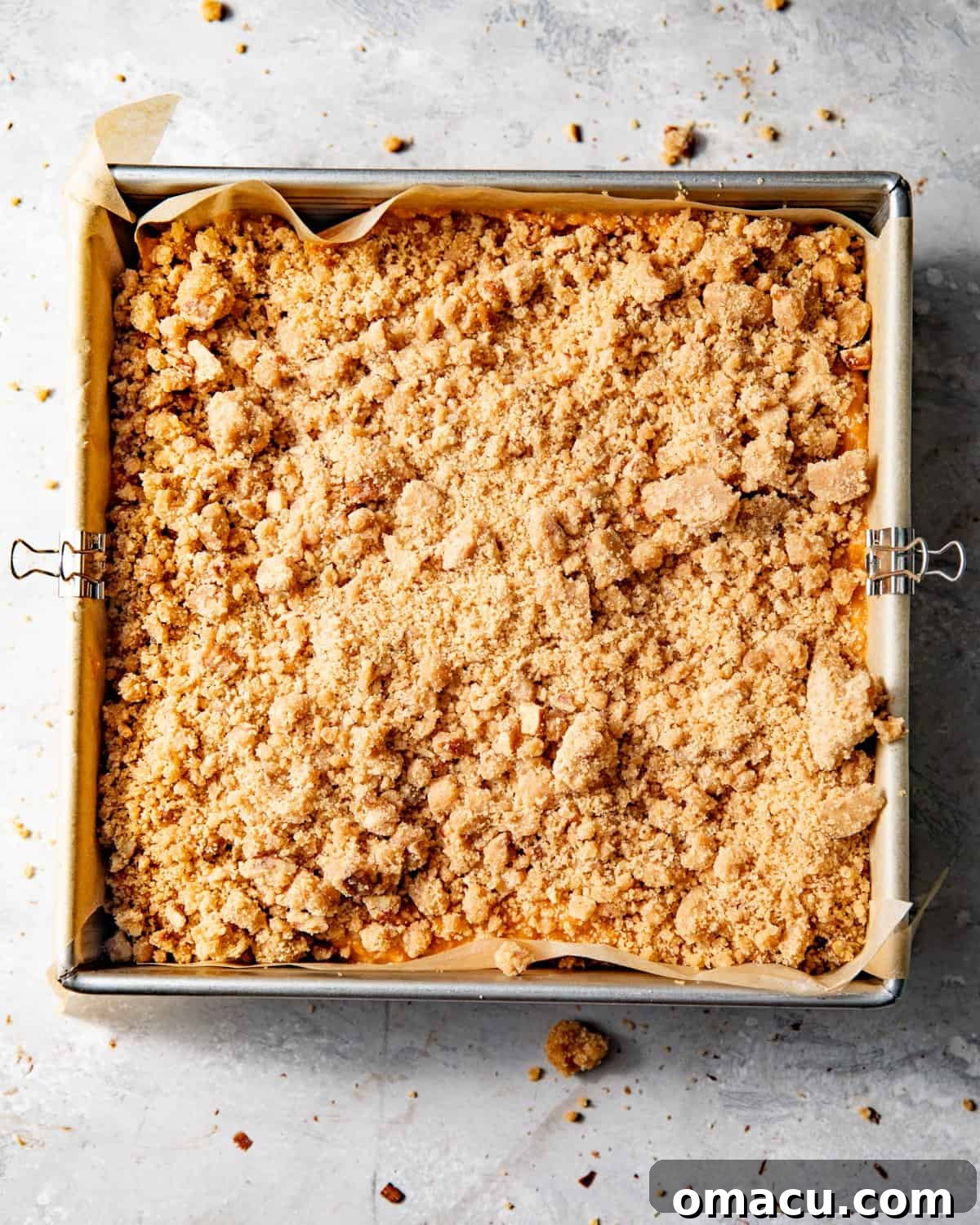 Sweet potato pie bars covered in a generous layer of pecan streusel, ready to be baked in the oven.