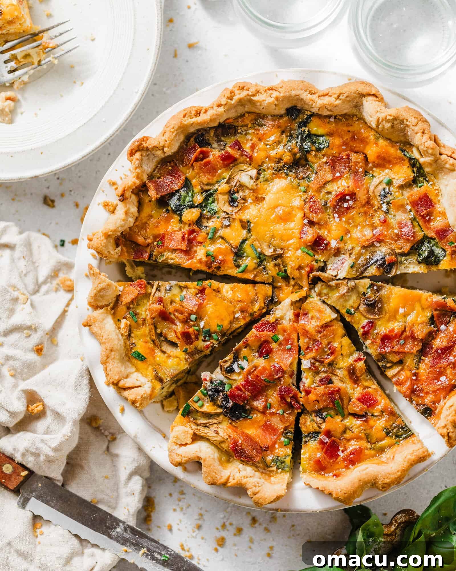A perfectly baked bacon mushroom spinach quiche in a golden pie dish, garnished with fresh herbs, with lemons in a bowl nearby, ready to be served.