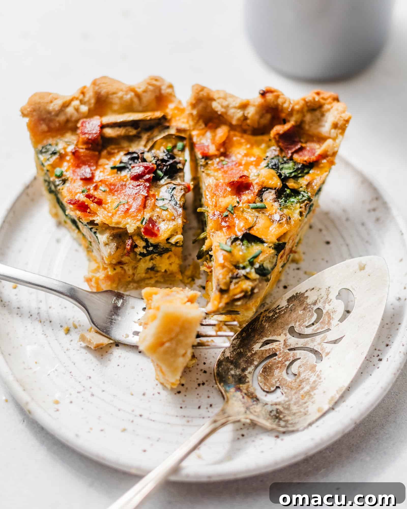 Two generous slices of bacon mushroom spinach quiche artfully arranged on a white plate, accompanied by a fork and a cake server, highlighting its inviting texture.