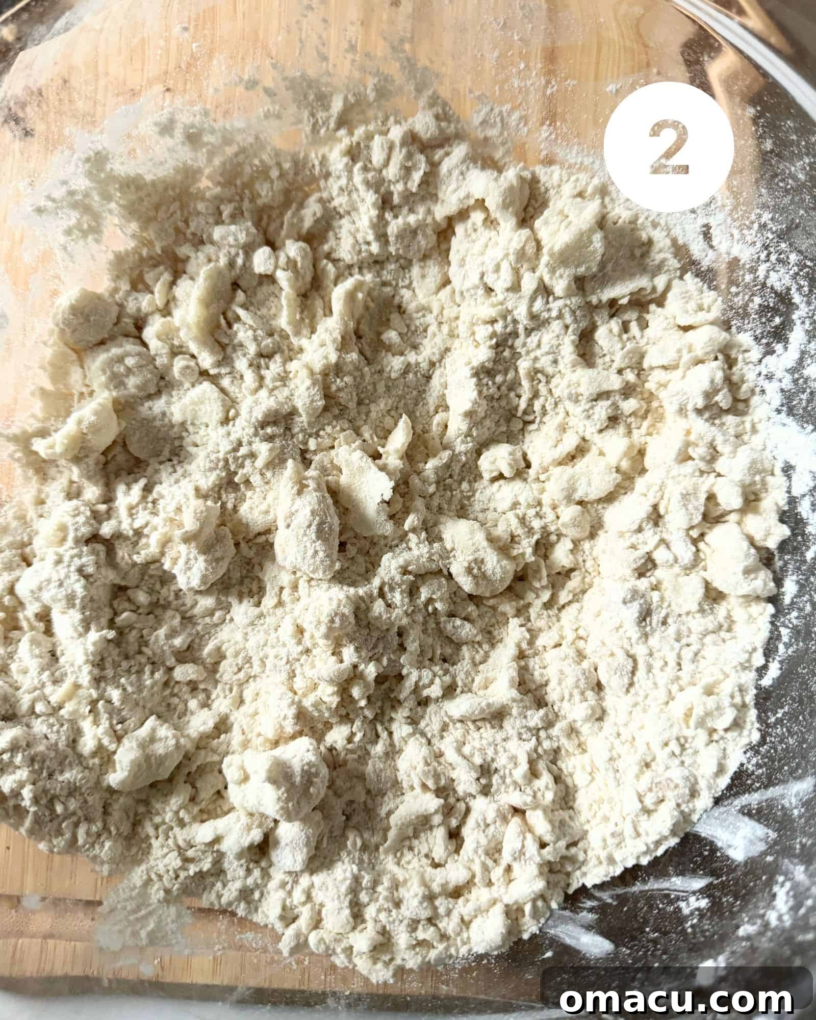 A large mixing bowl containing pie dough, visibly mixed with shortening and ice water, beginning to form a shaggy texture.