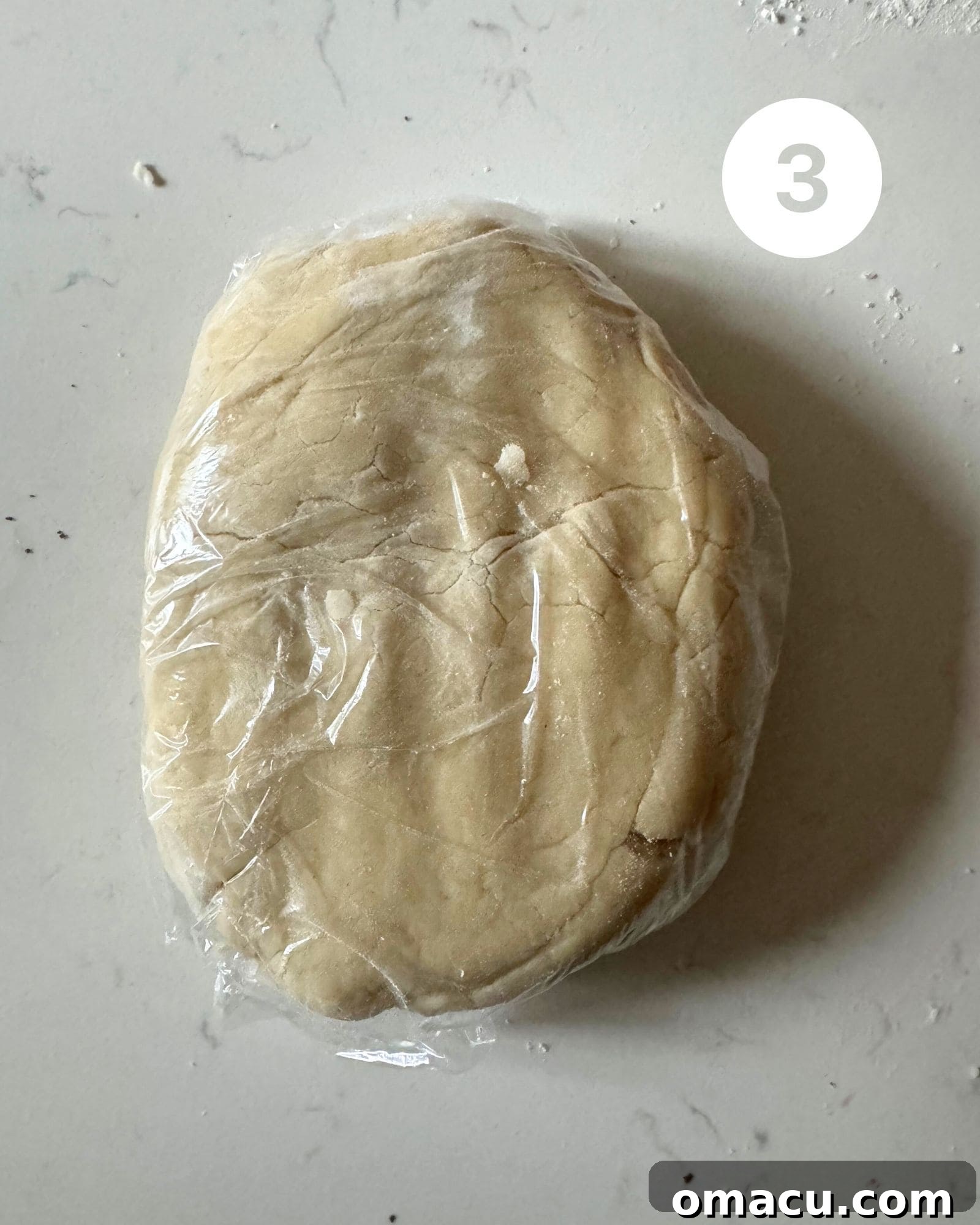 Pie dough, neatly wrapped in plastic film, resting on a clean white surface to chill before rolling out.
