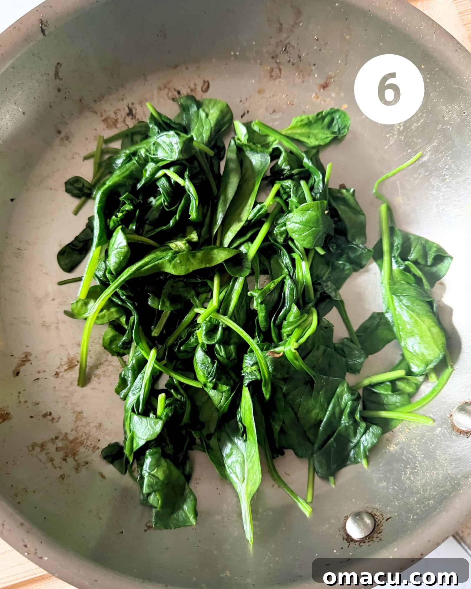 Vibrant green spinach, gently wilted, in a skillet after being sautéed, ready to be combined with other quiche ingredients.