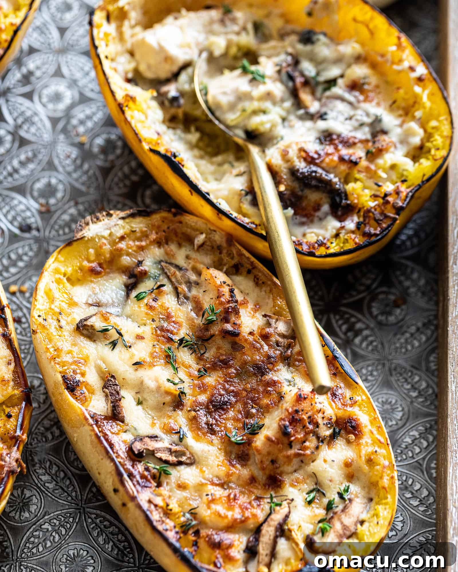 Two vibrant spaghetti squash halves generously filled with creamy Chicken Alfredo, topped with melted mozzarella and fresh thyme.