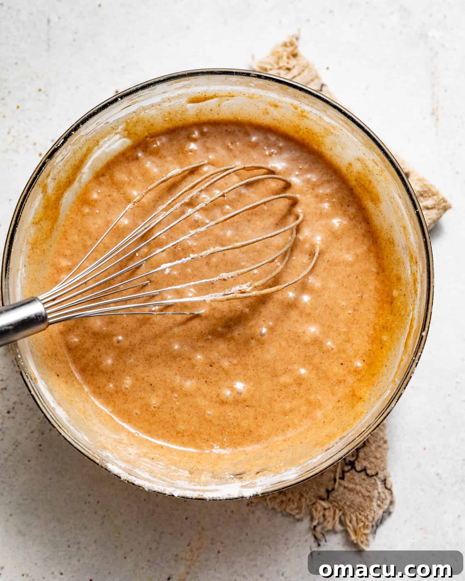 The wet ingredients for the Dutch Apple Cake, including sugars, melted butter, eggs, vanilla, and milk, being whisked together in a separate mixing bowl.