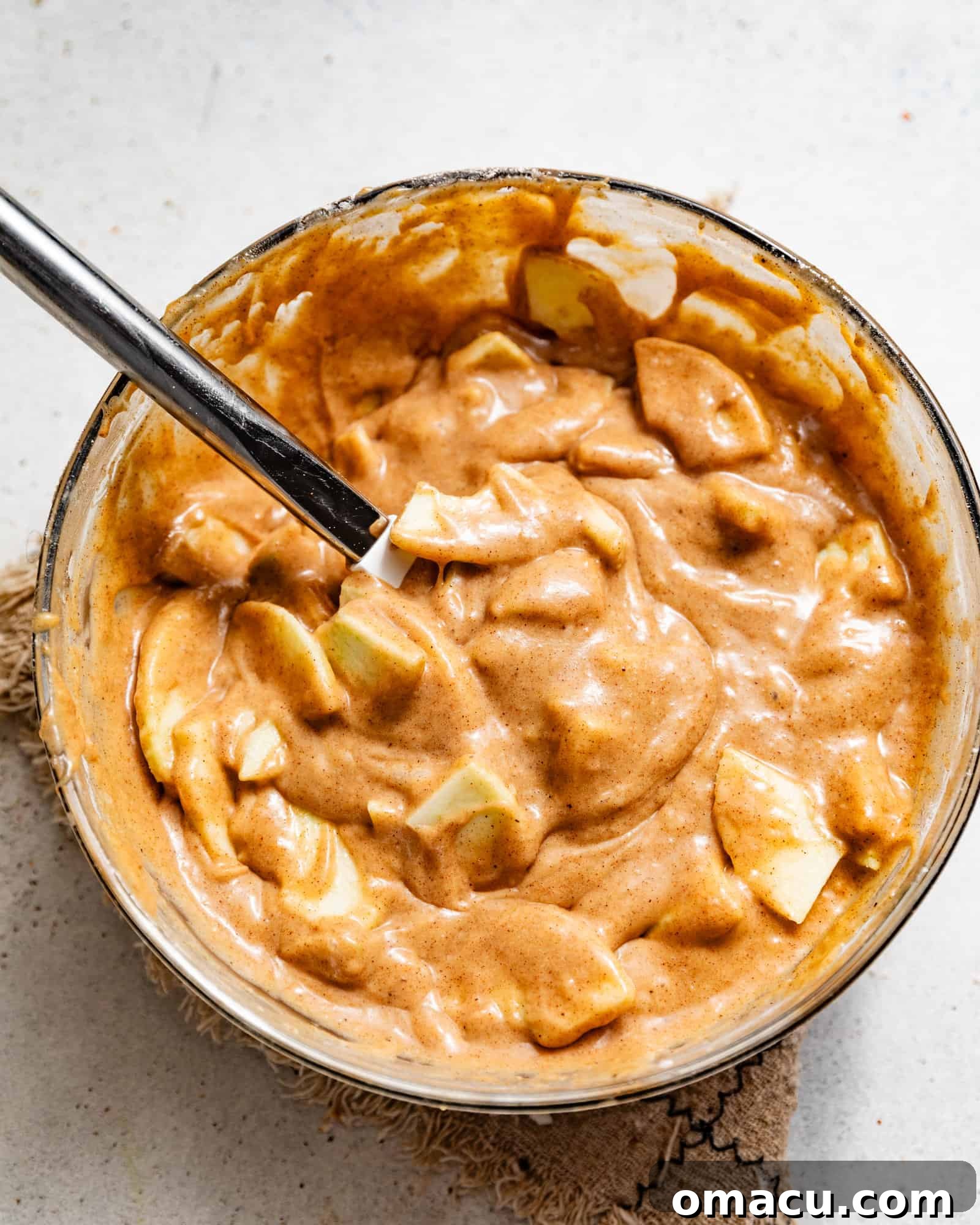 Moist apple cake batter in a mixing bowl with fresh, peeled apple slices gently folded in, ready to be transferred to the baking pan.