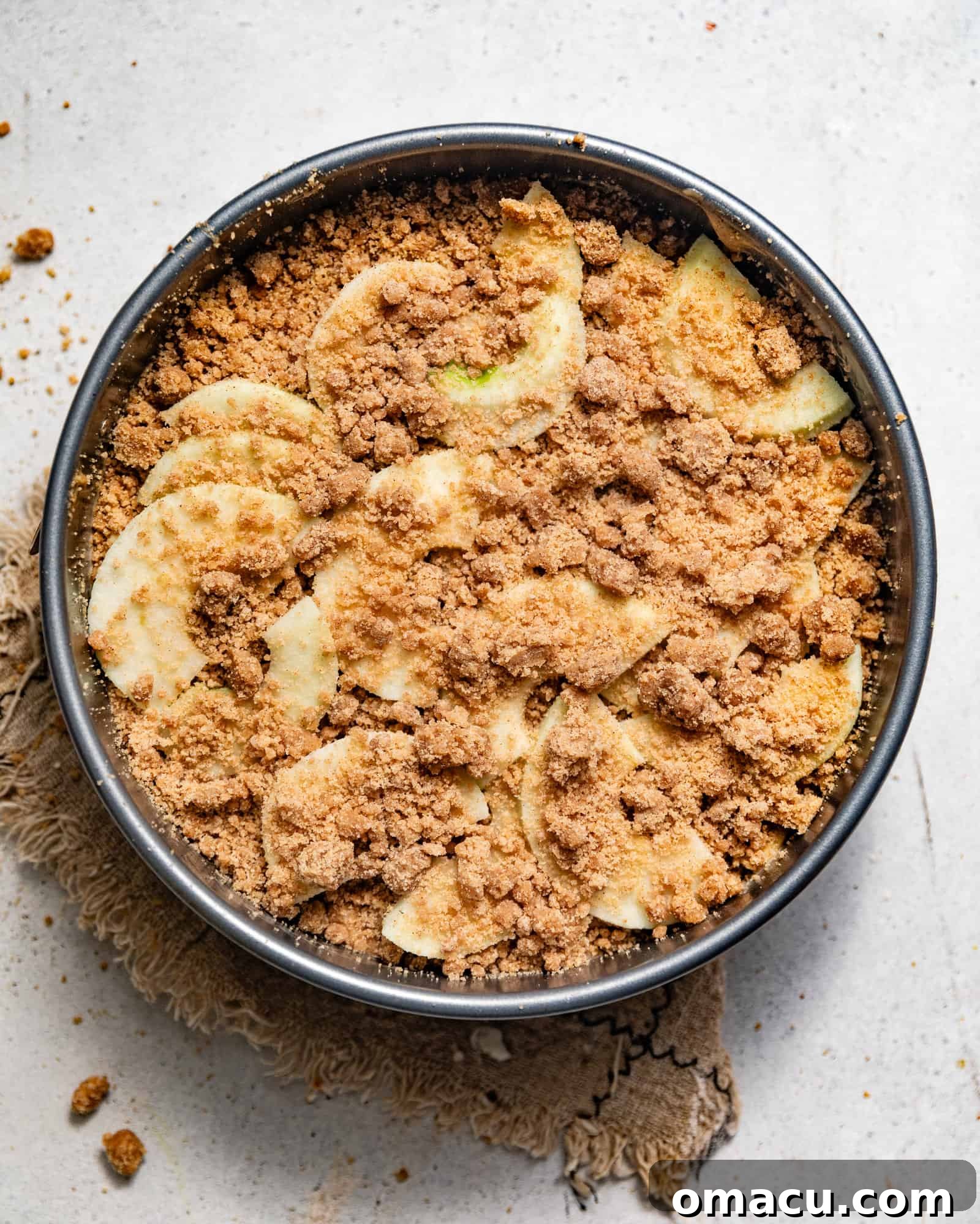 Dutch Apple Cake batter poured into a springform pan, topped with remaining apple slices and a generous layer of crumb streusel, ready for baking.