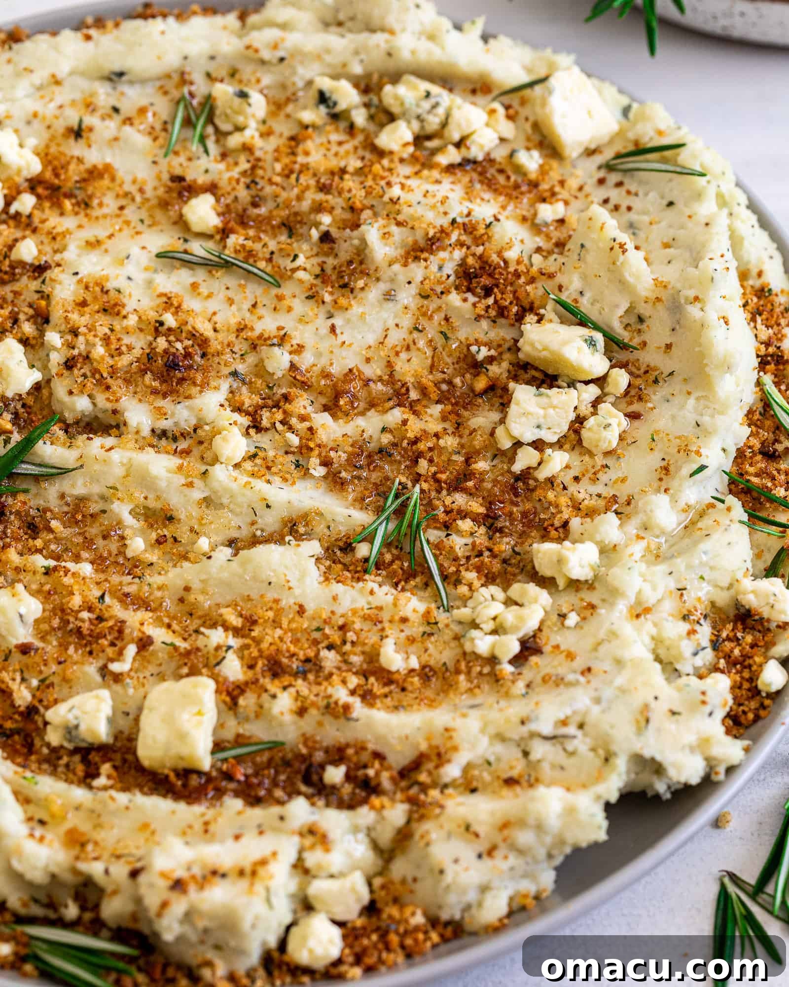 Close-up view of fluffy mashed potatoes, perfectly seasoned and topped with fresh rosemary for garnish.