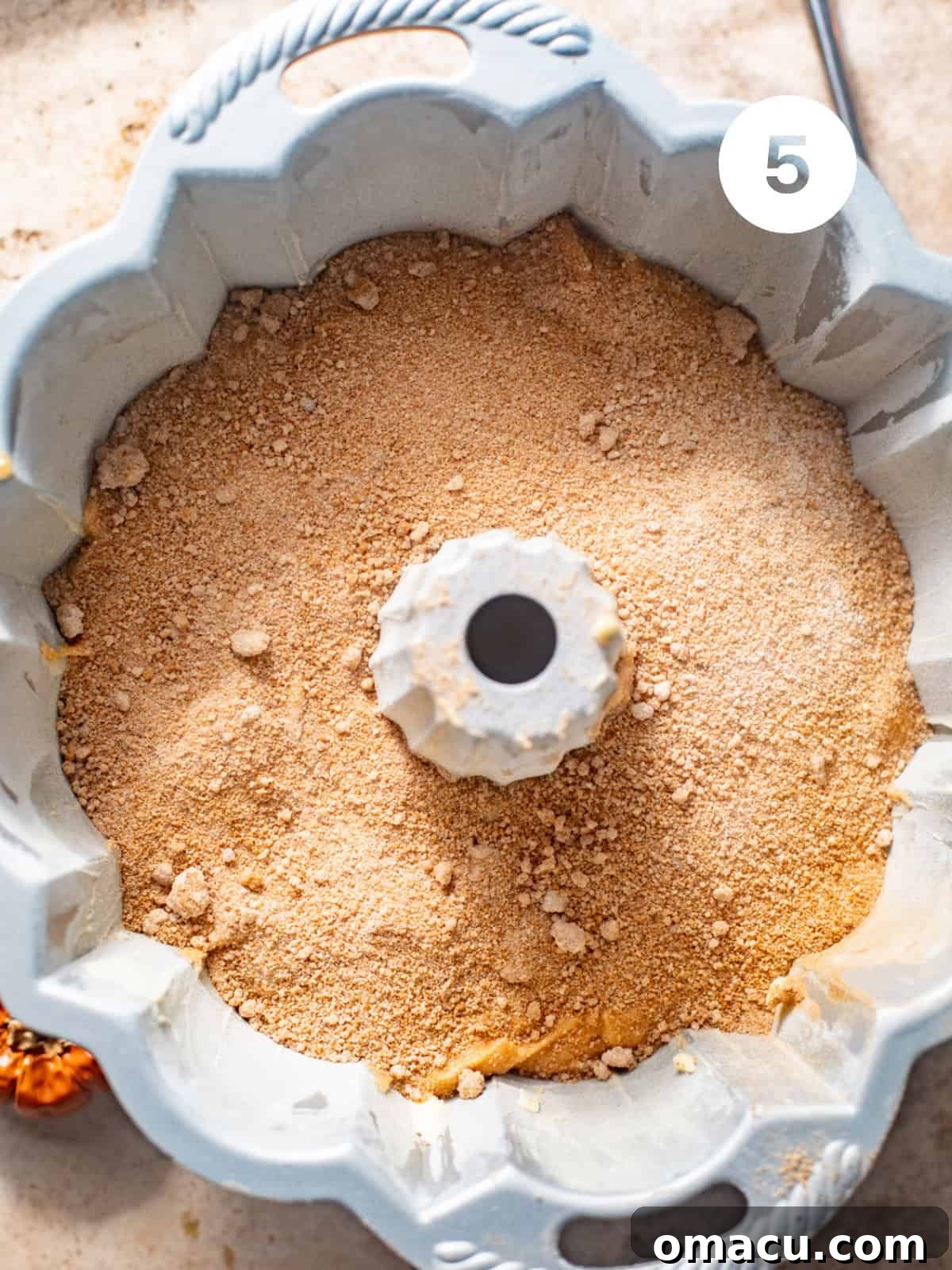 Half of the sweet potato pound cake batter in a bundt pan topped with cinnamon sugar, awaiting the remaining batter.